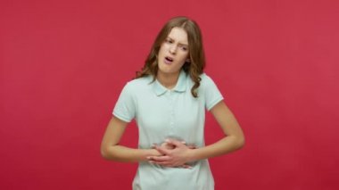 Gastrobağırsak sorunları. Polo tişörtlü hasta bir kadın hazımsızlık çekiyor, karın ağrısı çekiyor, karnını sıkıyor ve mide ekşimesi geçiriyor. Kırmızı arkaplanda izole edilmiş kapalı stüdyo çekimi
