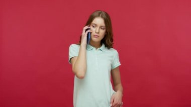 Cep telefonu, cep telefonu ve gezintide hoş sohbetler. Polo tişörtlü, cep telefonuyla konuşan, gülümseyen, arkadaşlarıyla sohbet eden genç ve güzel bir kadın. Kırmızı arkaplanda izole edilmiş kapalı stüdyo çekimi