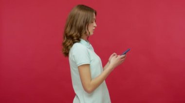 Mobil iletişim. Polo tişörtlü esmer bir kadının mesaj yazışının yan görüntüsü ya da akıllı telefon kullanarak internette sohbet etmesi, okuma haberlerine şaşırdığını gösteriyor. Kırmızı arkaplanda izole edilmiş kapalı stüdyo çekimi