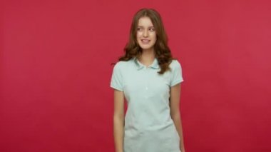 Polo tişörtlü neşeli ve enerjik genç bir kadın kırmızı arka planda dışarı çıkıyor, yukarı ve aşağı, duygusal olarak reklamcılık ve başparmaklar için etrafta dolanıyor. Stüdyo çekimi izole