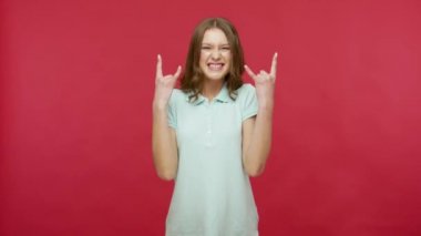 Heyecanlı, polo tişörtlü genç esmer kadın rock 'n roll işareti gösteriyor ve çılgınca kükreyerek şeytan boynuzları yapıyor, saldırganlık gösteriyor. Kırmızı arkaplanda izole edilmiş kapalı stüdyo çekimi