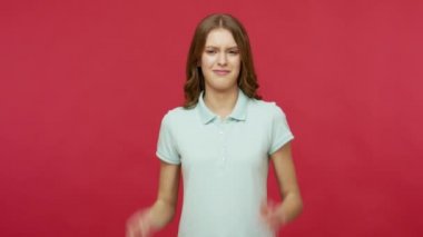 Dinlemek istemiyorum! Polo tişörtlü itaatsiz genç bir kadın can sıkıcı ifadelerle kulaklarını kapatıyor, diğer fikirlerden rahatsız oluyor ve tavsiyeleri görmezden geliyor. Kırmızı arkaplanda izole edilmiş kapalı stüdyo çekimi