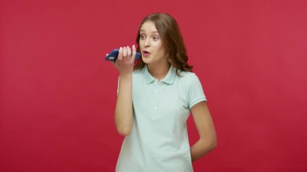 语音助理 穿着Polo T恤的年轻女性在手机上做音频记录 与手机交谈 使用虚拟助手 数字扬声器应用在网上搜索信息 被隔离的工作室 — 图库视频影像