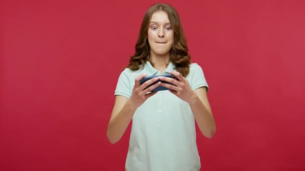 移动娱乐应用 年轻的黑发女性则在手机上玩电子游戏 笑着玩电脑游戏 情绪化地享受游戏的乐趣 在红色背景下隔离的室内拍摄 — 图库视频影像