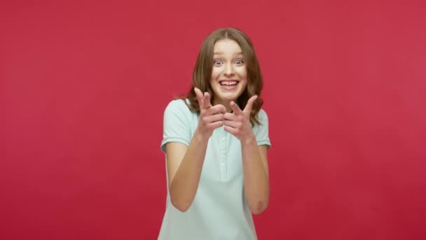 おいお前が必要だ 幸せな陽気な若いブルネットの女性がポロシャツで指をカメラに向け 方向性を示し 気づき 幸運な勝者を選ぶ 赤の背景に隔離された屋内スタジオで — ストック動画