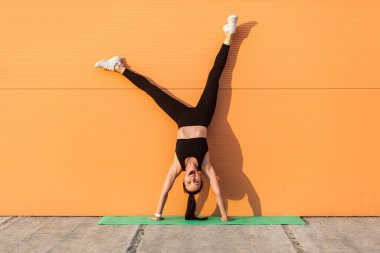 Aşırı mutlu, sportif vücudu sıkı olan, yoga yapan, duvara yaslanıp gülen, mutluluktan bağıran bir kız. Vücut dengesi için jimnastik açık hava egzersizleri