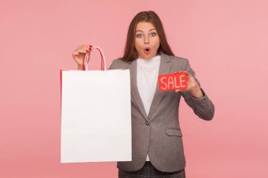 Vay canına, moda mağazasında indirim! Heyecanlı, takım elbiseli iş kadınının portresi şok olmuş görünüyor ve satış sözcüğünü tutuyor. Reklam metni için içinde fotokopi yeri olan alışveriş torbaları. Stüdyo çekimi