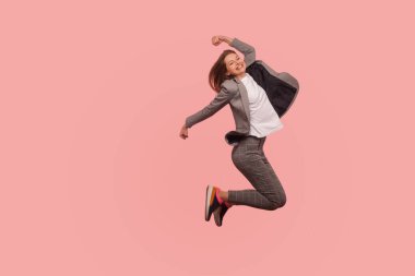 Ben şampiyonum! Havada kaygısız atlayan, başarıdan esinlenerek uçan, hedef başarısını kutlayan zarif takım elbiseli mutlu iş kadını portresi. Stüdyoda çekim izole edildi