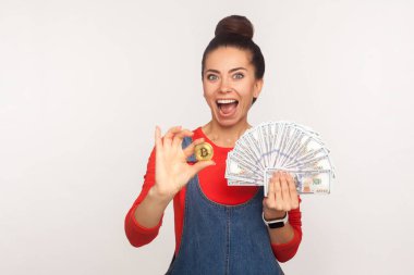 Wow yatırımlar, dijital para! Üzerinde altın bitcoin ve dolar banknotları olan kot pantolonlu, saçları topuz gibi olan, şaşkın bir kızın portresi. Stüdyo çekimi beyaz arkaplanda izole edildi