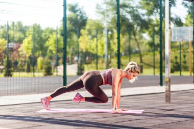 Uzun boylu, dar pantolonlu atletik bir kadın yaz günü paspas üzerinde antrenman yapıyor, karın kasları egzersizi yapıyor, dizlerini değiştiriyor, aerobik pilates yapıyor. Sağlık, spor faaliyetleri