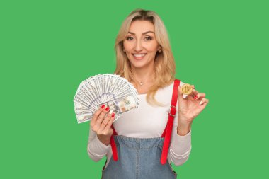 Dijital yatırım. Dolarlar ve btc bozuk para taşıyan şık kot pantolon giymiş mutlu ve güzel bir kadının portresi. Bitcoin 'e karşı nakit para. Yeşil arka planda izole edilmiş kapalı stüdyo çekimi