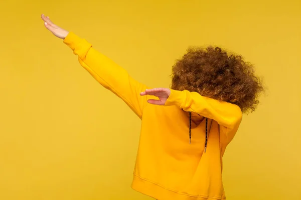 穿着都市风格帽衫的卷发女青年的肖像 带着舞姿 表现出互联网上成功的迷因 涉猎潮流 在黄色背景下隔离的室内拍摄 — 图库照片