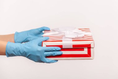 Kırmızı çizgili hediye kutusu taşıyan mavi eldivenli insan elinin profili. İçerde, stüdyoda, gri arka planda izole edilmiş..