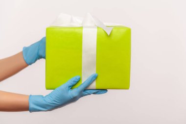 Profil yan görüntüsü, elinde yeşil hediye kutusu olan mavi eldivenli insan eli. Paylaşım, verme veya teslim etme kavramı. İçerde, stüdyoda, gri arka planda izole edilmiş..