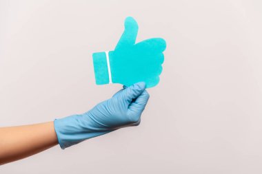 Profil yan görüntüsü, insan elinin mavi cerrahi eldivenlerle çekilmiş ve kağıt şeklindeki işaretleri gösteriyor. İçerde, stüdyoda, gri arka planda izole edilmiş..