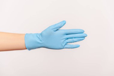 Profilde insan elinin mavi cerrahi eldivenli yakın çekimi selamlaşmaya ya da dokunmaya yardımcı oluyor. İçerde, stüdyoda, gri arka planda izole edilmiş..