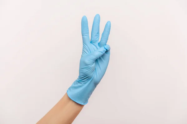 手で3番目を示す青い外科用手袋の人間の手のプロフィール側のビューの閉鎖 屋内スタジオ撮影灰色の背景に隔離された — ストック写真