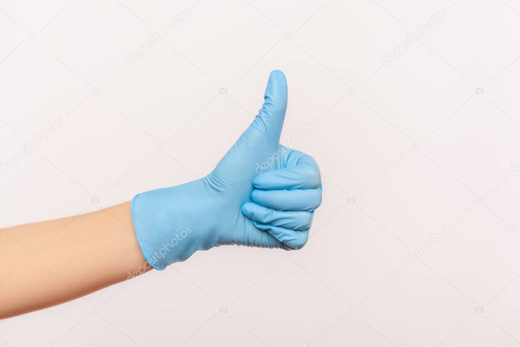 Profile side view closeup of human hand in blue surgical gloves showing like or thumbs up. indoor, studio shot, isolated on gray background.