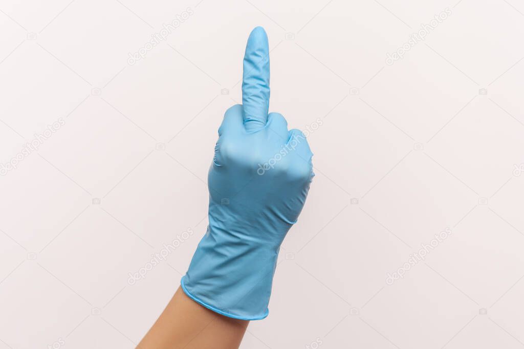 Profile side view closeup of human hand in blue surgical gloves showing middle finger. indoor, studio shot, isolated on gray background.