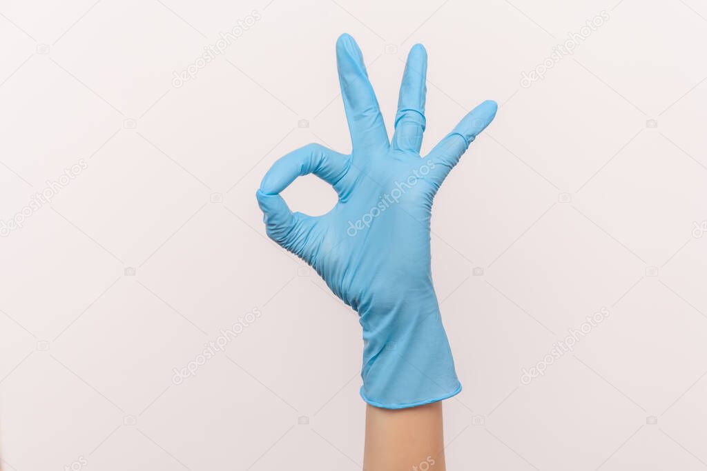 Profile side view closeup of human hand in blue surgical gloves showing Ok sign or number 3 with fingers. indoor, studio shot, isolated on gray background.