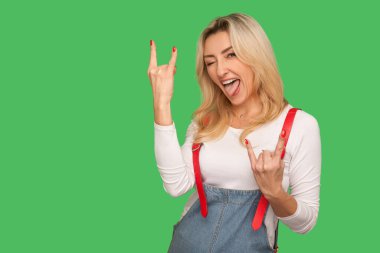 Bu çok saçma! Zevkli yetişkin kadın portresi. Şık kot pantolon içinde. Rock 'n Roll jesti gösteriyor. Yeşil arka planda izole edilmiş kapalı stüdyo çekimi