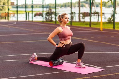 Paspasın üzerinde spor formundaki kız eğitimi, bacak kaslarını esnetirken dizlerini desteklemek için köpük masajı aleti kullanmak, fasya egzersizi yapmak. Antrenman öncesi ısınma rutini, sağlık hizmetleri