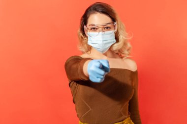 Koronavirüse karşı koruma. Hijyenik yüz maskesi, eldiven ve koruyucu gözlük takan, kamerayı işaret eden, viral hastalığı önlemek için tavsiye veren, 2019-ncov salgını tehdidi