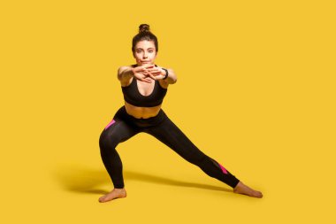Spor kıyafetleri içinde, spor kıyafetleri içinde atletik, güzel bir kız spor yapıyor, vücut egzersizi yapıyor, ellerini uzatıyor, esneklik için kaslarını ısıtıyor. Tam boy stüdyo çekimi, sarı renkte izole edilmiş.