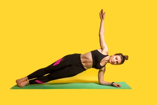 横板がポーズ タイトなスポーツウェアの練習ヨガで若いフィットネス女性 片手でVasisthasana運動をやって 筋肉を訓練 スタジオショット黄色の背景に隔離されたスポーツワークアウト — ストック写真