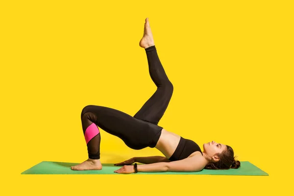 タイトなスポーツウェアの練習ヨガでフィットネスの女の子は 脚を上げると1本の足の橋のポーズを行い 筋肉を訓練し 柔軟性の練習 屋内スタジオショット黄色の背景に隔離されたスポーツワークアウト — ストック写真