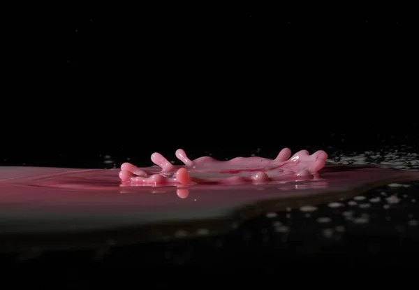 Water splashing: drops falling into pink liquid and splashing all around. Black background is used to give some contrast.