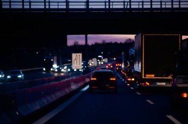 Alman A6 karayolunda trafik sıkışık. Gün batımında ayakta duran araba ve kamyonların gürültülü ama güzel renkli fotoğrafı..