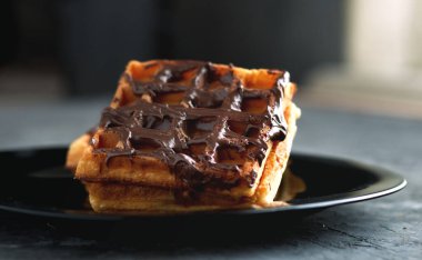 Siyah bir tabakta çikolatalı waffle.