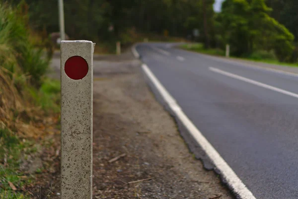 Reflector de luz en color rojo sobre poste blanco a un lado de la carretera — Foto de Stock