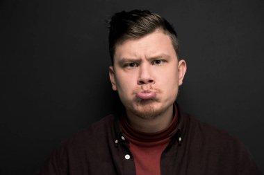 Gri arka planda soyutlanmış somurtan genç bir adamın portresi.