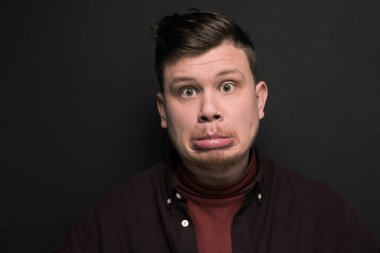 Gri arka planda soyutlanmış somurtan genç bir adamın portresi.