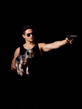 Kollarında küçük sevimli bir köpek olan genç bir sporcu. Bir silahtan istiyor. Siyah bir arkaplanda izole edilmiş.