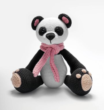 Güzel el yapımı oyuncak. Örgü örmüş küçük bir hayvan. Boynunda eşarp olan bir panda. Gri bir arka planda. Tığ işi doldurulmuş hayvanlar..