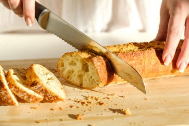 Lezzetli, taze, çıtır çıtır ekmek. Güzel kadın elleri, ekmek kesmek için bir bıçak ve yakın çekim ekmeği. Kesme tahtasındaki süslü ürün. Sağlıklı yeme kavramı.
