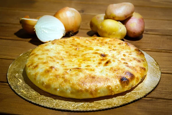 Osetijský koláč s bramborami a cibulí. Tradiční pokrm z etnické kavkazské kuchyně. Těsto s náplní na pozadí starého dřevěného stolu. Koncept chutného a zdravého jídla. — Stock fotografie