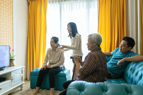 Happy asian family,father,mother,daughter,and senior grandmother relaxing,watching movies dramas series on TV,enjoying watch television and laughing in living room at home,lifestyle,weekend activities
