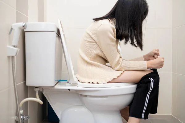 Menina asiática sentar-se no banheiro com as calças para baixo no banheiro com sofrimento de constipação, diarréia ou hemorróidas, mulher estressada sentir estômago doloroso, não poderia obter o poo para fora, cuidados de saúde — Fotografia de Stock