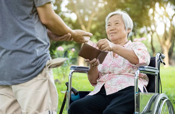 Asiatisk man med pengaproblem, kräver pengar, arbetslös man ber om pengar från äldre kvinna, mamma drar villigt ut fickpengar från plånboken för att ge sin son, moderskap — Stockfoto