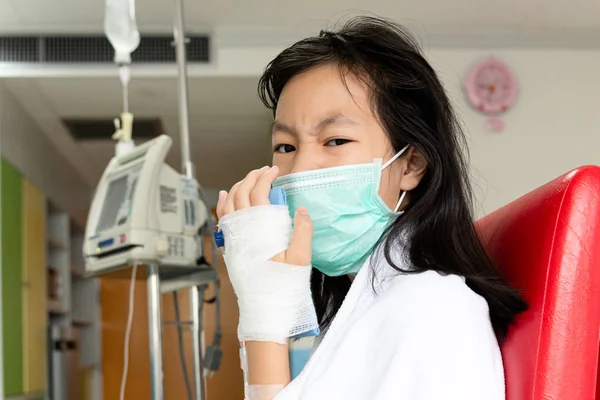 Больная азиатская девочка с медицинской маской, страдающая кашлем, лечение от физраствора с помощью контроллера физраствора или инфузионного насоса, пациентка в палате больницы, страдающая гриппом, здравоохранение, медицинская концепция — стоковое фото