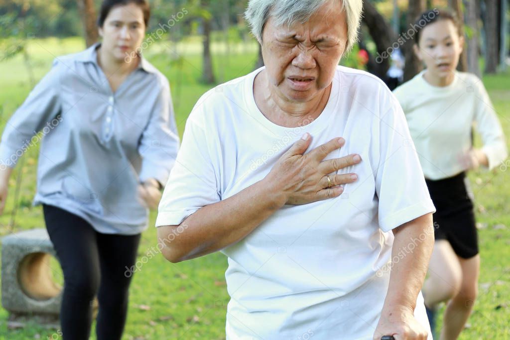 Asian elderly woman having difficulty breathing suffer from heart attack,heart problem while walking exercise at park, daughter and granddaughter are running to help,senior mother feeling chest pain