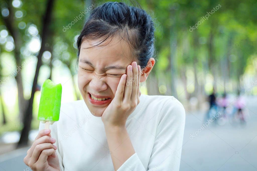 Asian child girl holding her hand on her aching tooth have hypersensitive teeth eating ice-cream,feel painful,female teenage have sensitive teeth problem with ice-lolly,tooth decay,dental care concept