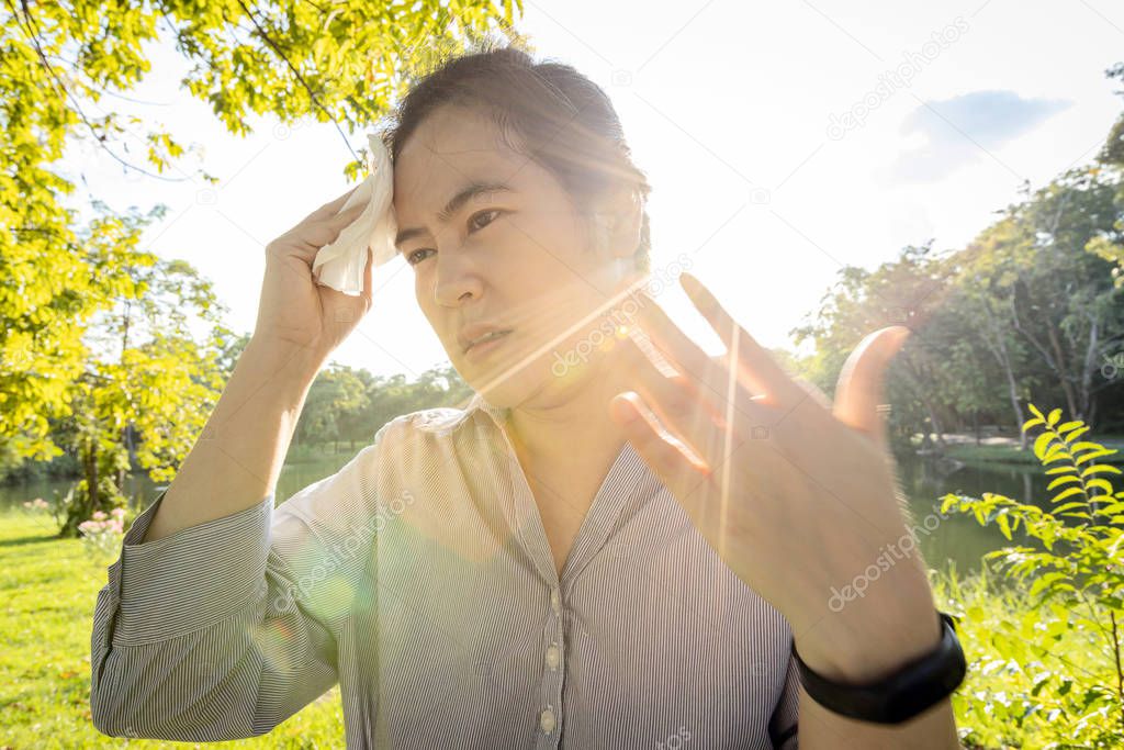 Asian woman wiping sweat on face with tissue paper suffer from  sunburn very hot in summer weather problem feel faint, tired female people with heat stroke,high temperature on sunny day,global warming
