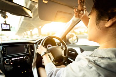 Asian female driver covering face by hand of bright sun,disturbed dazzled by sun light,difficulty in driving,young woman driving car feeling hot uncomfortable,risk of eye damage from ultraviole,UV ray clipart