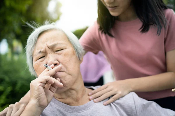 Asiatiska äldre mormor håller en cigarett rökning, äldre människor eller rökare rökning nära barnbarn, barn flicka begära äldre kvinna att sluta röka, dålig lukt, lukt förorening, hälsovård, livsstil — Stockfoto