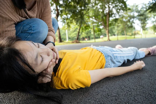 Enfermo hija adolescente se desmayó y cayó en el suelo mientras jugaba en el parque, ayuda madre asiática, cuidar, niña con insuficiencia cardíaca congestiva, mujer inconsciente acostado en el suelo sufren un ataque al corazón —  Fotos de Stock